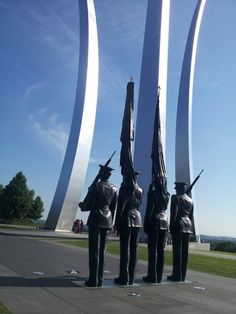 three statues of soldiers holding flags in front of two tall white pillars with blue sky behind them