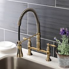 a kitchen sink with a brass faucet next to a white plate and purple flowers