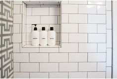 three bottles of hand sanitizer sitting on a shelf above a tiled wall in a bathroom