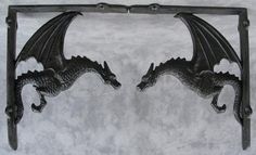 two black metal dragon brackets on a gray wall with white clouds in the back ground