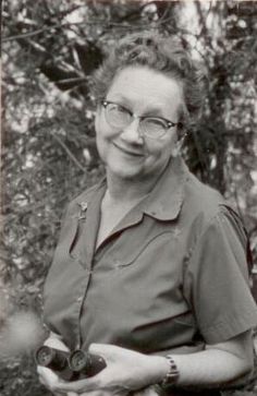 an old black and white photo of a woman with glasses holding two small objects in her hands