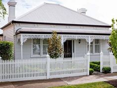 a white house with a picket fence and trees in the front yard on a sunny day