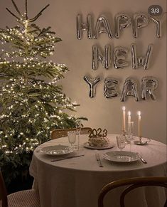 a table set for two in front of a christmas tree with balloons that say happy new year