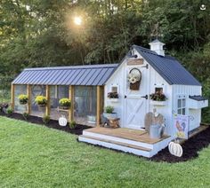 a small white chicken coop in the middle of a yard with flowers and potted plants