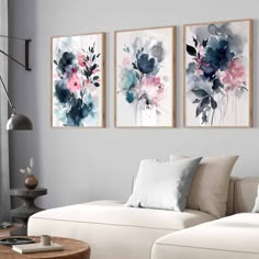 three paintings hang on the wall above a couch in a living room with white furniture