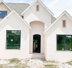 a large white brick house with two windows and a woman standing in the front door