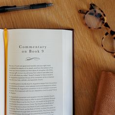 an open book sitting on top of a wooden table next to a pair of glasses