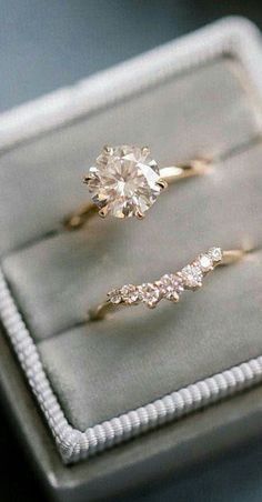 two engagement rings sitting on top of a velvet ring box, with one diamond in the middle