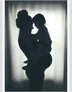 the silhouette of a woman holding a baby in her arms, with curtains behind her