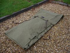 a sleeping bag is laying on the ground in front of some grass and gravel,