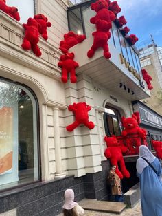 red teddy bears hanging from the side of a building with people looking at them outside