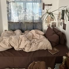 an unmade bed sitting in front of a window next to a potted plant