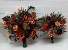 two bridal bouquets with orange and red flowers are on the white wooden wall