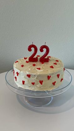 a birthday cake with two candles on it sitting on a glass plate in front of a white wall