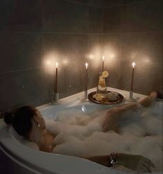 a woman laying in a bathtub with candles on the side