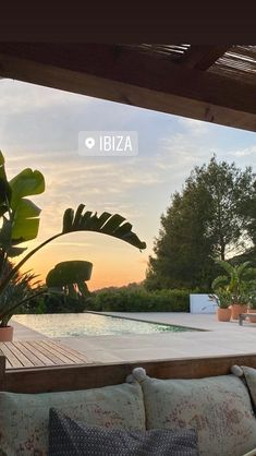 an outdoor living area with couches and potted plants at sunset, overlooking a swimming pool