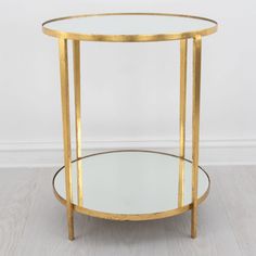 a round glass table with gold trimmings on the top and bottom, against a white wall