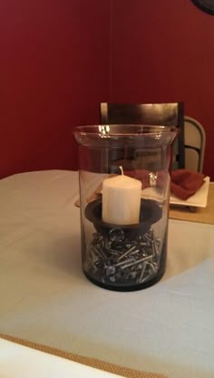 a lit candle sitting in a glass container on top of a white tablecloth covered table