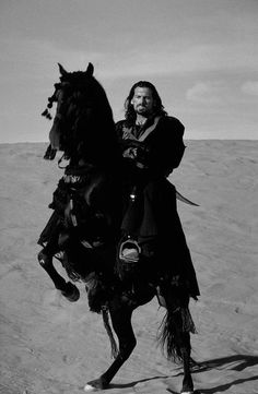 a man riding on the back of a horse across a desert covered with grass and dirt