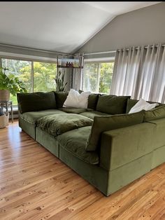 a large green couch sitting on top of a wooden floor next to a tall window