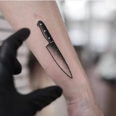 a knife tattoo on the arm of a person's left hand with black ink