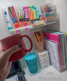 a person holding a red coffee mug in front of a shelf filled with office supplies