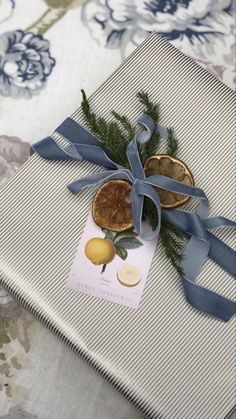 a gift wrapped in blue ribbon on top of a tablecloth with lemons and pine cones