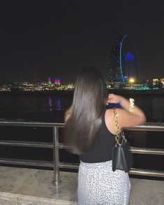 a woman standing on a bridge looking at the water and ferris wheel in the distance