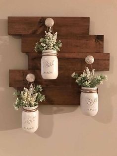 three mason jars with flowers are hanging on the wall