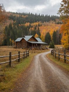 a dirt road leading to a log cabin surrounded by trees with fall foliage in the background