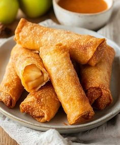 some fried food on a white plate with dipping sauce in the bowl and green apples behind it