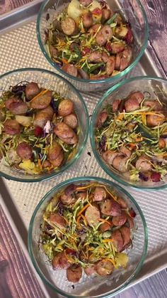 four glass bowls filled with food sitting on top of a metal tray next to a wooden table