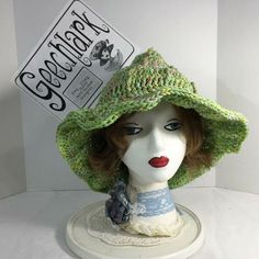 a white mannequin head with a green hat on it's head and a sign above it