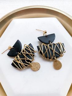 two black and gold earrings sitting on top of a white plate next to each other