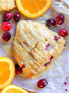 an orange and cranberry scones with icing on paper next to sliced oranges