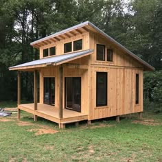 a small wooden house in the middle of a field with grass and trees around it