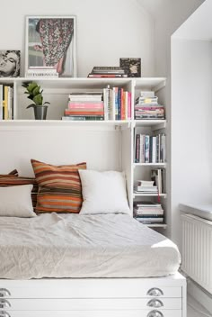 a white bed sitting under a window next to a book shelf