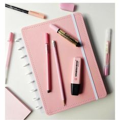 a pink notebook with pens and pencils on it