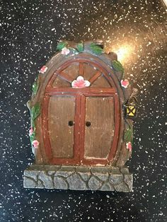 a small wooden door with flowers on the front and side, sitting on top of a black surface