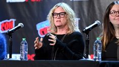 two women sitting at a table with microphones in front of them and one is speaking