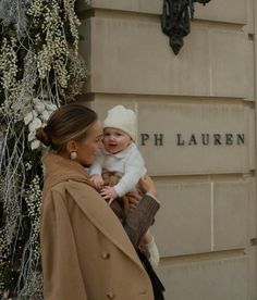 a woman holding a baby in front of a building with christmas decorations on the outside