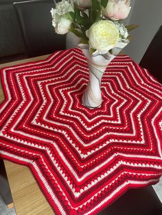 a crocheted table runner with white flowers in a vase on a wooden table