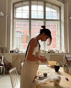 a woman standing in front of a window preparing food on a table with utensils