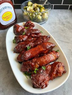 barbecue ribs on a white plate next to a bowl of olives and a jar of mustard