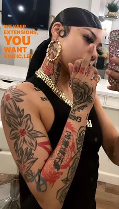 a woman with lots of tattoos on her arm and hand holding something in front of her face