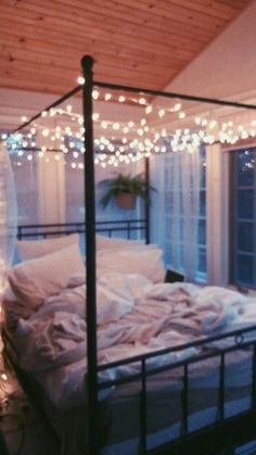 an unmade bed with lights strung from the ceiling