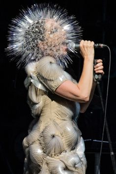 the woman is dressed as a creature with spikes on it's head and holding a microphone in her hand