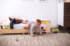 a baby crawling on the floor in front of a bed with stuffed animals and toys