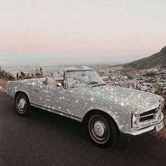 a car covered in silver glitters parked on the side of a road with mountains in the background