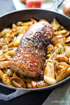 pork chops and onions in a skillet with an apple on the side for garnish